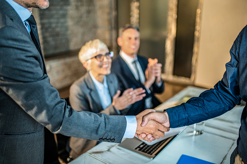 Happy business people making an agreement. Two unrecognizable businessmen shaking hands while two colleagues are applauding in the background.