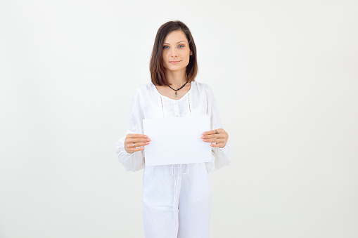 Attractive smiling and confident brown-haired woman in white clothes, posing and standing on white studio background, looking at camera. Showing empty blank template promo, banner for text. Copy space