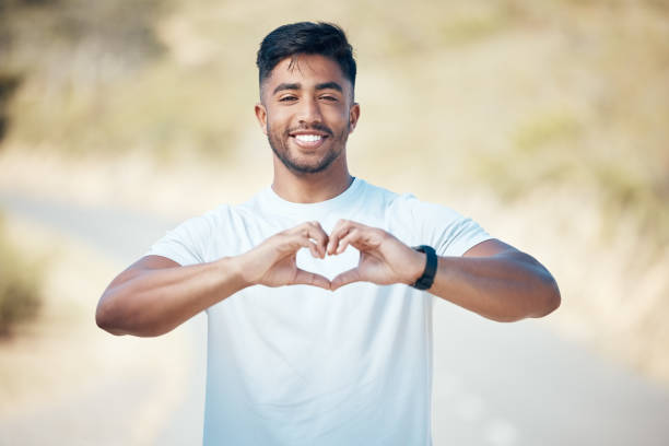 istock Portrait happy fit young mixed race man making a heart shape with his hands while exercising outdoors. Handsome indian man showing that he loves to work out, stay healthy and run outside in nature 1399382274