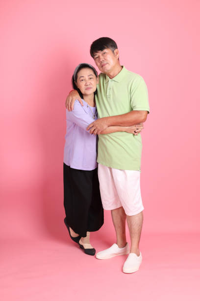 The senior Asian couple with casual clothes standing on the pink background.