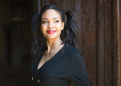Portrait of a fashionably dressed young black woman. She looks successful and happy. She stands in front of an old wooden door in Venice.