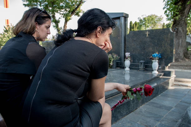 mother and her daughter in grief, mourning a deceased loved one on cemetery - funeral family sadness depression imagens e fotografias de stock