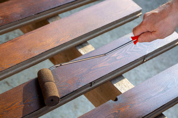 a man covers a wooden board with stain using a roller. hobby, carpentry. - treated wood imagens e fotografias de stock