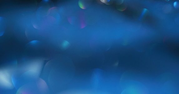Bokeh glow. Light flare overlay. Underwater reflection. Defocused neon colorful shiny circles gleam on dark blue abstract background.