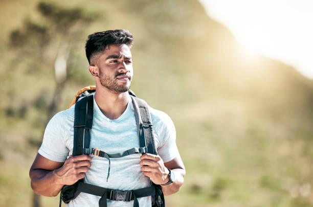 istock Athletic young mixed race man wearing a backpack taking a break during a hike. Fit handsome hispanic man standing outside and looking at the view while hiking outside in nature. An outdoor workout 1399392221