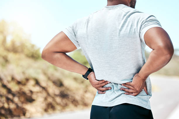 istock Closeup fit mixed race man holding his back in pain while exercising outdoors. Unrecognizable male athlete suffering with a muscle injury to his body. Every workout comes with risk of getting hurt 1399392536