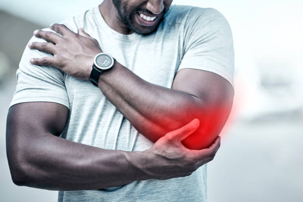 closeup fit mixed race man holding his elbow in pain while exercising outdoors. unrecognizable male athlete suffering with a joint injury highlighted by glowing cgi. you can get hurt during a workout - elbow imagens e fotografias de stock