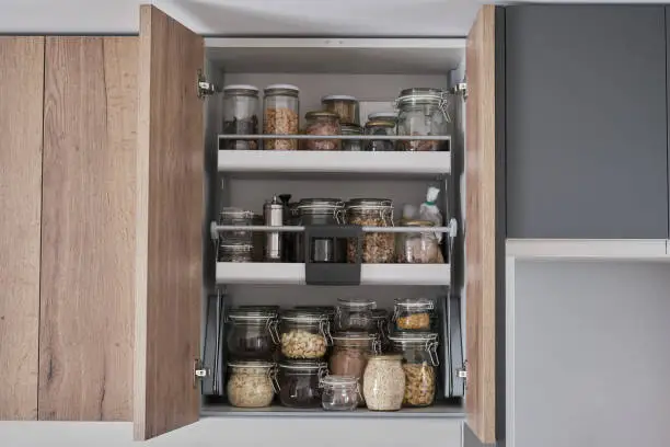 Photo of Variety of dry foods, grains, nuts, cereals in glass jars in kitchen cupboard.