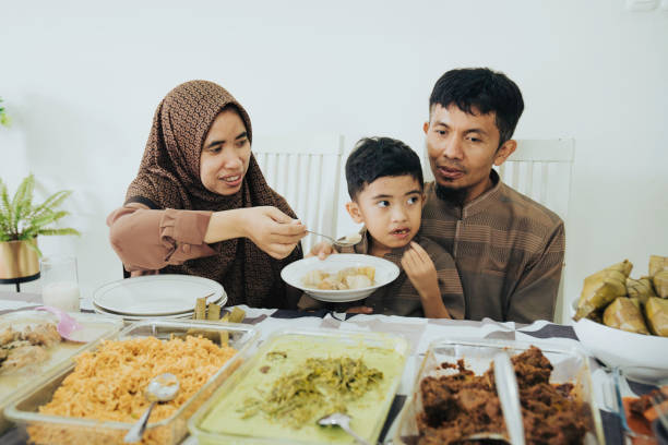 Asian family, celebrating Eid-Ul-Fitr, praying before enjoying meal together at home