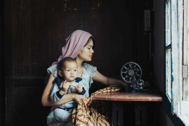 istock malay women stitching cloths by machine at home while her son playing beside her 1399394614