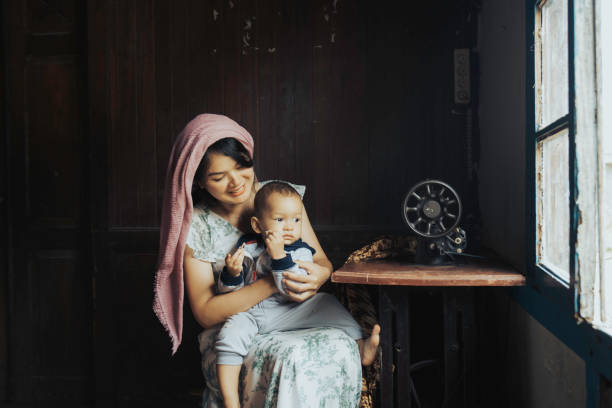 istock malay women stitching cloths by machine at home while her son playing beside her 1399394658