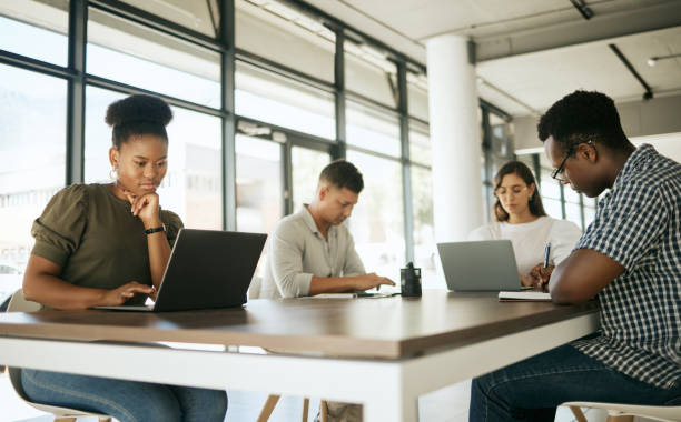 istock Diverse group of entrepreneurs business people working on laptops and writing notes while sitting around a table in a shared coworking office space 1399395723