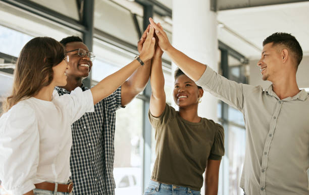 istock Young colleagues standing in office raising hands to give high five during team building. Diverse business team standing together at startup 1399395744