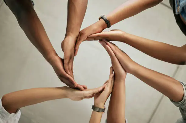 Close up of a group of colleagues putting hands together to form a circle in the office from below. Creative team joining hands and showing unity in teamwork