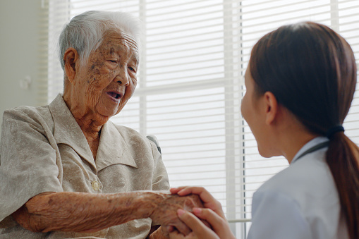 Asian doctor holding senior patient hand for encouragement and empathy, medical trust and support concept