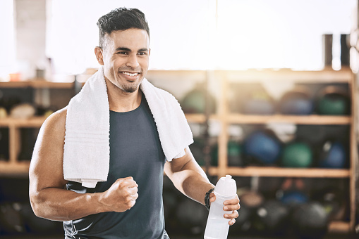 Happy trainer cheering in the gym. Fit, strong man taking a break from his workout. Bodybuilder using a towel after his exercise routine. Sporty athlete enjoying his workout routine.