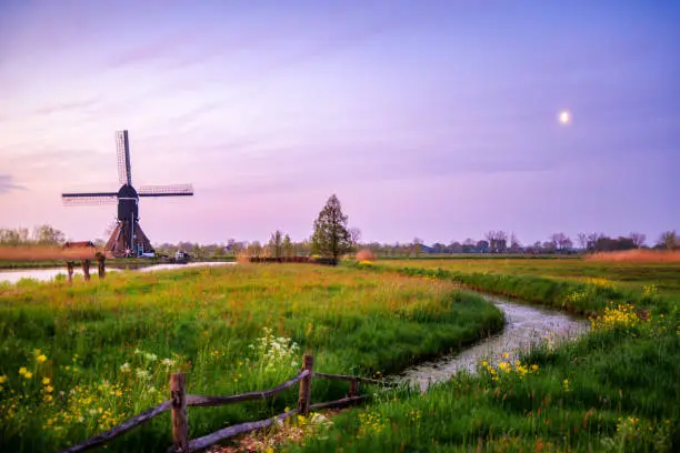 typical dutch landscape in Overslingeland early in the morning with windmill in front of river canal with a cloudy sky with the moon, South Holland