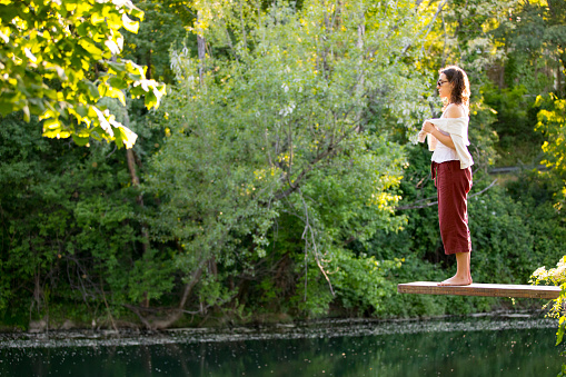 Portrait of Young Woman Standing on Diving Board Above River.