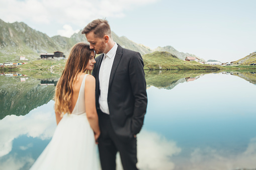 The bride and groom standing against lake background. Backdrop of rocky mountains. Family lifestyle concept. Travel concept.
