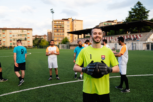 Portrait of a goalkeeper with other players in the background. He's holding a soccer ball and looking at camera.