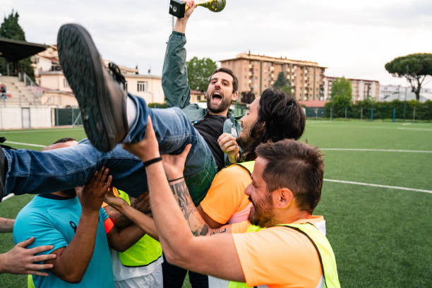 Soccer team players are celebrating with their coach. The coach is holding a cup.
