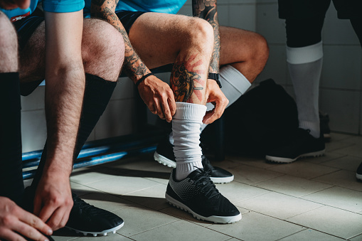 Soccer team players are getting ready in the changing room before the match. They are dressing. Detail of a tattooed man.
