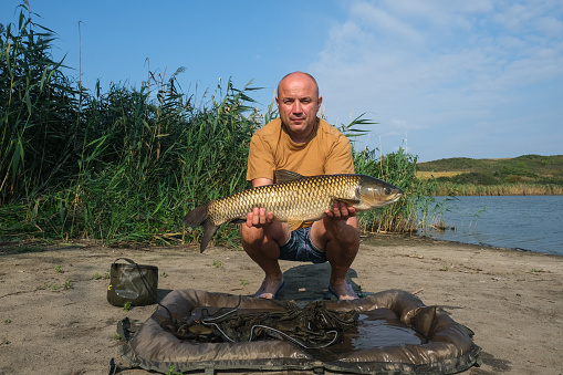 Happy angler with big fish trophy in hands. Success carp fishing