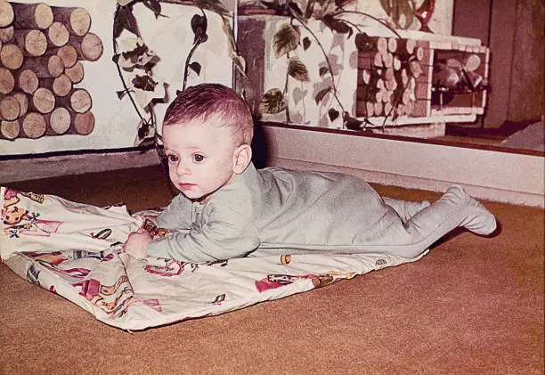 A vintage grainy image of a cute baby boy laying down at home. Vintage photo from the sixties.