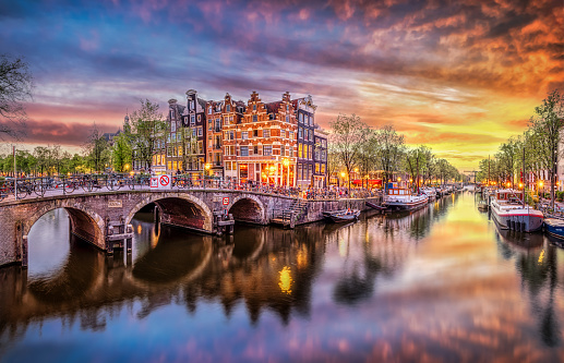 Sunset in Amsterdam. Panoramic view of the historic city center of Amsterdam. Traditional houses and bridges of Amsterdam town. A romantic evening and a bright reflection of houses in the water. European travel to the historic city. Europe, Netherlands, Holland