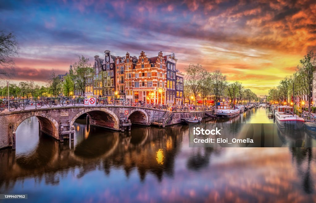 Panoramic view of the historic city center of Amsterdam. Traditional houses and bridges of Amsterdam town. A romantic evening and a bright reflection of houses in the water Sunset in Amsterdam. Panoramic view of the historic city center of Amsterdam. Traditional houses and bridges of Amsterdam town. A romantic evening and a bright reflection of houses in the water. European travel to the historic city. Europe, Netherlands, Holland Amsterdam Stock Photo