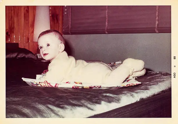 A vintage grainy image of a cute baby boy laying down on his parent's bed.