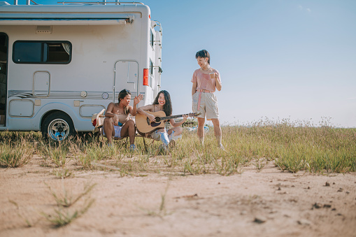 Asian chinese lesbian couple and friends singing, dancing playing guitar enjoying outdoor camping beside motor home