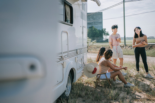 Asian chinese lesbian couple and friends resting beside motor home parked at lawn enjoy bonding time
