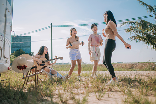 Asian chinese lesbian couple and friends singing, dancing playing guitar enjoying outdoor camping beside motor home