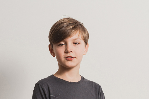 a portrait of cute boy saying something, looking at camera, dark grey shirt, white wall background. Copy space for your text and design