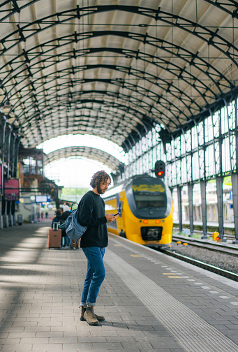 Young Caucasian man using smartphone while  waiting for the train on railway station