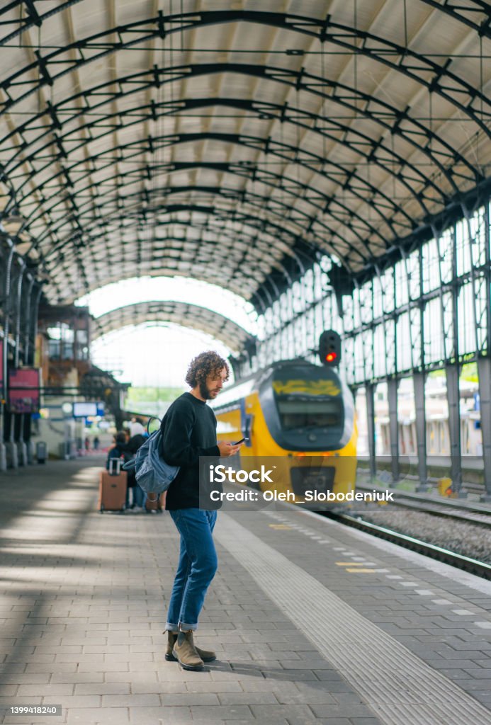 Man waiting for the train on railway station Young Caucasian man using smartphone while  waiting for the train on railway station Railroad Station Stock Photo