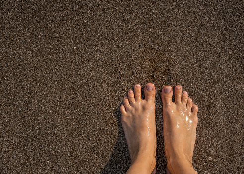 Mature woman feet close up to the surf with flip flops and fancy rhinestone nails