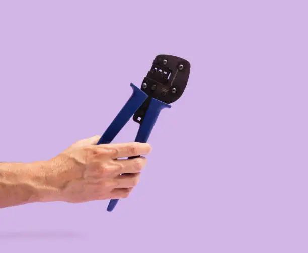 Photo of Man hand holds hand crimping tool purple background