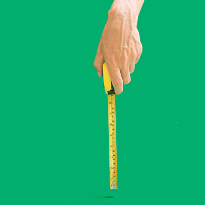 Man hand holds tape measure in inches and centimeters to measure length. Plastic coated steel blade. Hands measuring, Green background