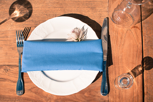 Wedding or another catered event table setting, white plate, blue napkin, Event decoration, outdoors