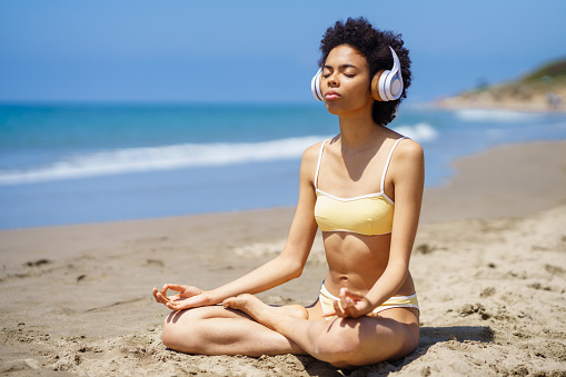 Black female in lotus pose doing mindfulness listening to a meditation with wireless headphones.