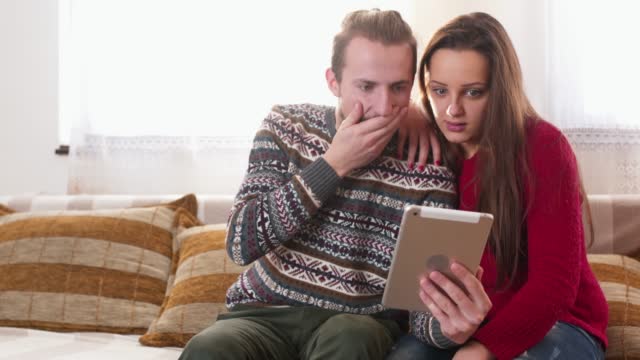 A Couple Sitting on a Sofa Watching Shocking Content on Tablet