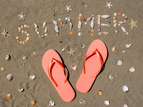 A close-up of beach accessories - straw hat, straw bag, flip-flops, denim shorts, pink sunglasses on the sand beach with the sea waves in the background