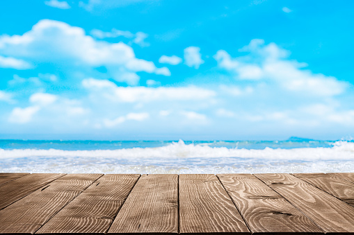 Summer abstract backgrounds. Empty wooden table at the bottom of the frame with defocused blue sky and beach at background. Diminishing perspective on table. Focus on table. Copy space, ideal for product montage.