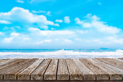 Summer abstract backgrounds. Empty wooden table at the bottom of the frame with defocused blue sky and beach at background. Diminishing perspective on table. Focus on table. Copy space, ideal for product montage.