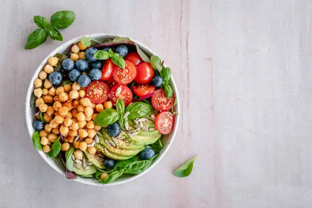 Overhead view of a bowl of colorful vegan chickpea salad located on the left side on a minimal background