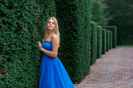 A beautiful blond female in a blue dress in a manicured public garden