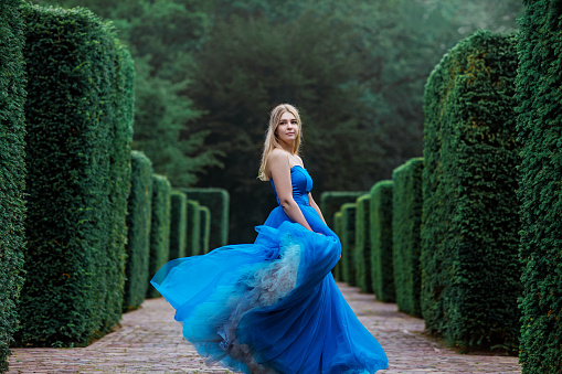 A beautiful blond female in a blue dress in a manicured public garden