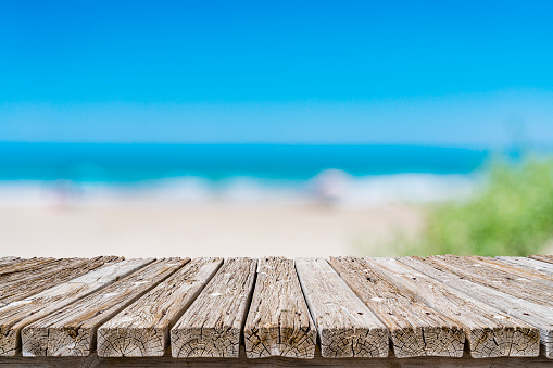 Summer abstract backgrounds. Empty rustic wooden table at the bottom of the frame with defocused blue sky and tropical beach at background. Diminishing perspective on table. Focus on table. Copy space, ideal for product montage.